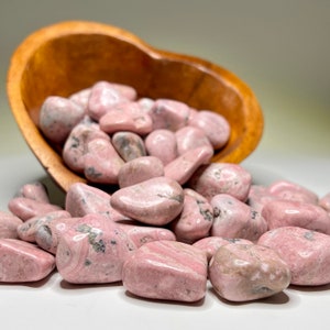 May include: A wooden bowl filled with pink and white tumbled stones. The stones are smooth and have a natural, organic look.
