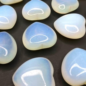 A collection of heart shaped blue and white opalite stones on a black surface.