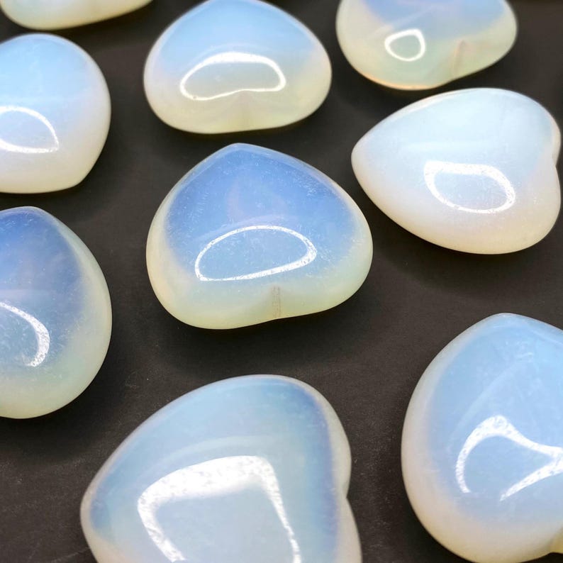A collection of heart shaped blue and white opalite stones on a black surface.