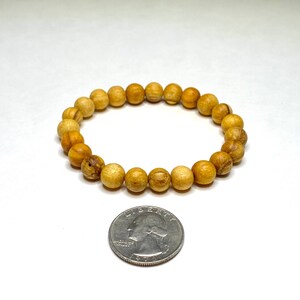 A wooden bead bracelet with a light brown color. The bracelet is made of round beads and is approximately the size of a US quarter.