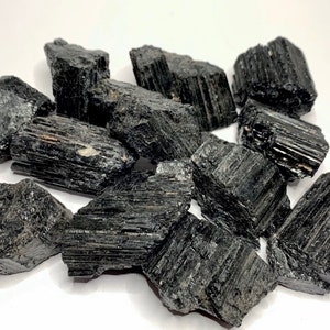 A collection of black tourmaline crystals, also known as schorl, with a striated, rough texture. The crystals are various sizes and shapes, and have a dark, opaque appearance.