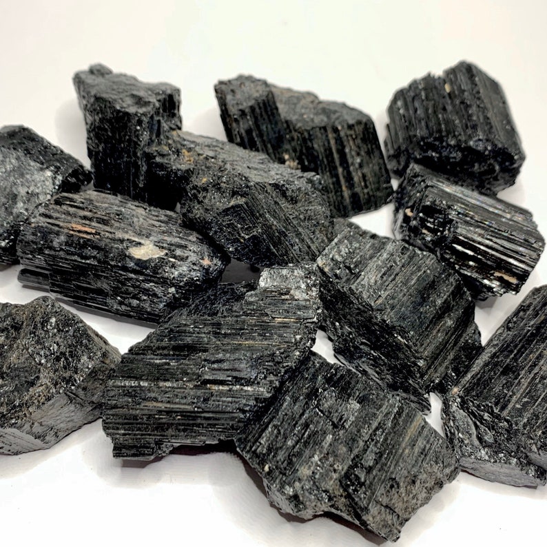 A collection of black tourmaline crystals, also known as schorl, with a striated, rough texture. The crystals are various sizes and shapes, and have a dark, opaque appearance.