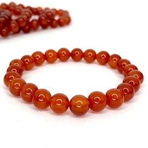 May include: A close-up of a bracelet made of polished, round, amber-colored beads. The beads are strung together on an elastic band. Another similar bracelet is slightly out of focus in the background. The background is white.