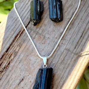 Puede incluir: Un conjunto de collar y pendientes de turmalina negra. El collar tiene una cadena larga de plata con un colgante de turmalina negra. Los pendientes son de plata con piedras de turmalina negra.