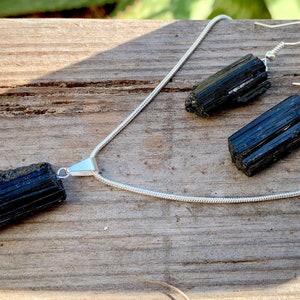 Puede incluir: Un conjunto de collar y pendientes de turmalina negra con cadenas de plata. El collar presenta un gran colgante de turmalina negra en bruto. Los pendientes son simples aros de plata con peque&ntilde;as piedras de turmalina negra en bruto.