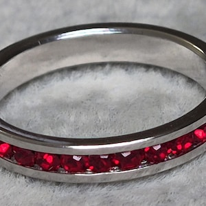May include: A silver ring with a band of vibrant red gemstones. The ring's polished metal reflects light, highlighting the rich color of the gemstones. This piece of jewelry is a classic design, suitable for various occasions.