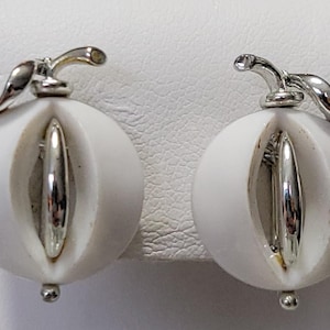 May include: A pair of white and silver earrings. Each earring features a white, orb-shaped design with a vertical silver accent. A silver stem and leaf detail tops each earring, with a small silver ball at the bottom.