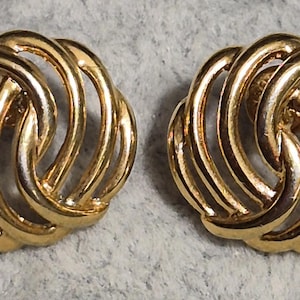 Peut inclure: Une paire de boucles d'oreilles rondes de couleur or. Chaque boucle d'oreille présente un motif tressé avec de multiples sections incurvées et ouvertes. Les boucles d'oreilles ont une finition brillante.