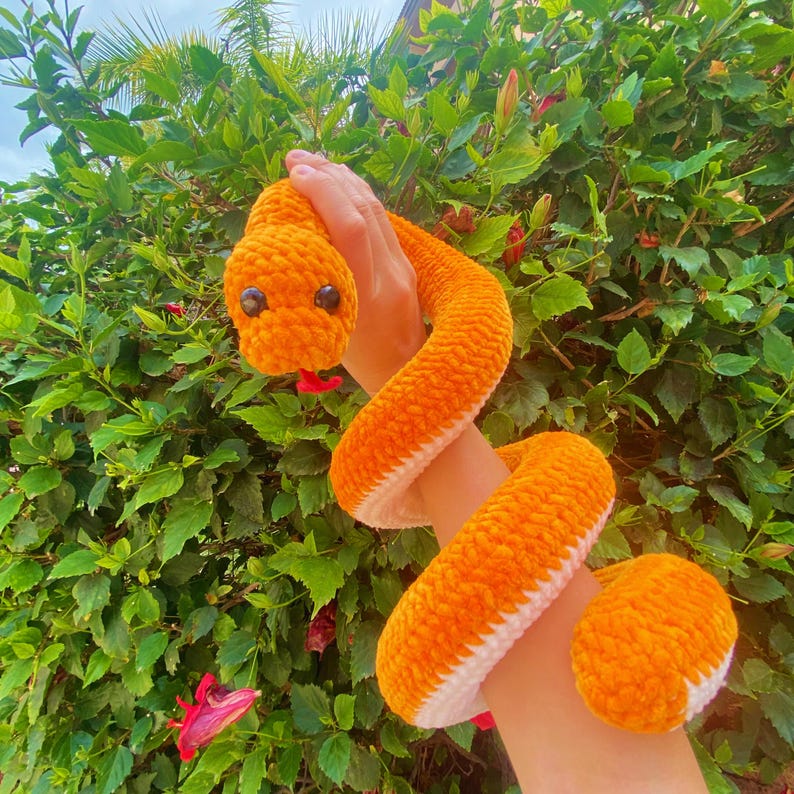 May include: A crocheted orange and white snake plush toy. The snake is curled up and has black eyes.