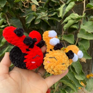 May include: Two handmade crochet plush toys: a red and black ladybug and a yellow and black bumblebee. The ladybug has black spots and the bumblebee has white accents. Both have closed eyes and are held in a hand.