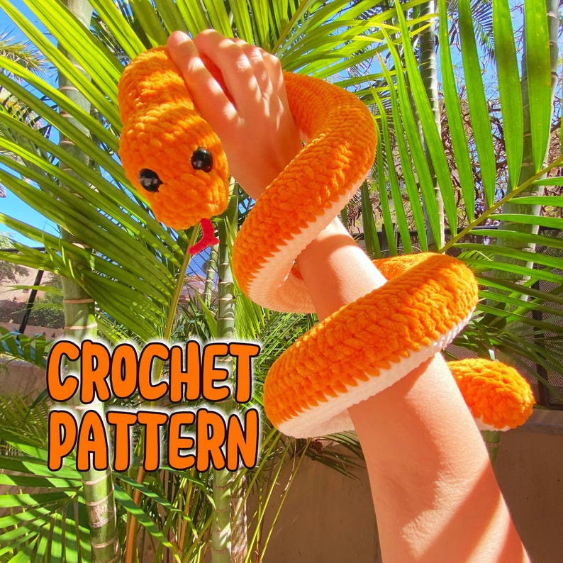 May include: A crocheted orange snake with white accents. The snake is coiled around a person's arm. The image includes the text "CROCHET PATTERN".