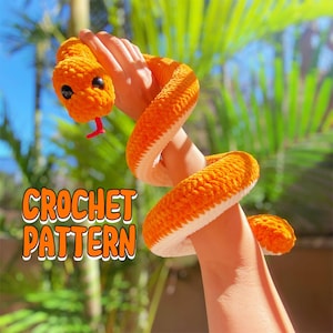 Puede incluir: Una serpiente de color naranja tejida a crochet con detalles blancos. La serpiente está envuelta alrededor del brazo de una persona. El texto "CROCHET PATTERN" es visible en la imagen.