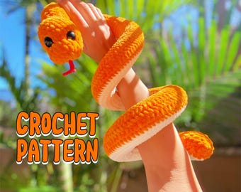 May include: A crocheted orange snake with white accents. The snake is wrapped around a person's arm. The text "CROCHET PATTERN" is visible in the image.