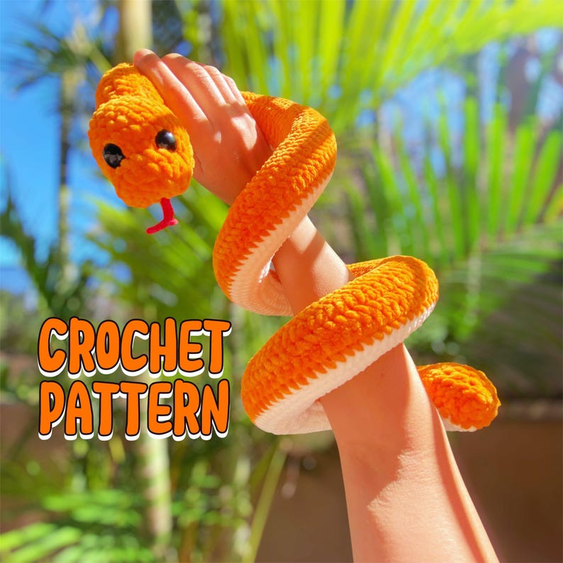 May include: A crocheted orange snake with white accents. The snake is wrapped around a person's arm. The text "CROCHET PATTERN" is visible in the image.