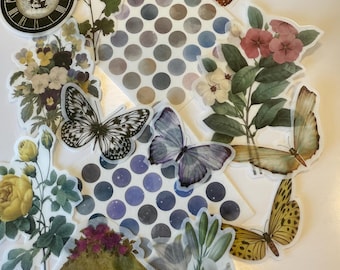 May include: A collection of vintage-style stickers featuring floral designs, butterflies, and polka dots. The stickers are printed on clear, translucent paper and have a distressed, aged look. The stickers include a clock face with the text "Brighton, UK", a floral bouquet, a butterfly with black and white wings, a butterfly with purple and white wings, a butterfly with yellow and brown wings, a floral design with pink flowers, a floral design with white flowers, and a polka dot pattern in shades of blue and gray.