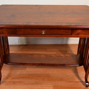 May include: A rectangular wooden table with a dark cherry finish. The table has a single drawer with a brass knob, a lower shelf, and curved legs. The table is approximately 30 inches long, 20 inches wide, and 28 inches high.