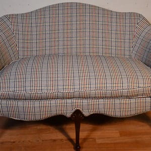 May include: A small, two-seater sofa with a plaid fabric upholstery in shades of blue, red, and white. The sofa has a curved back and wooden legs.