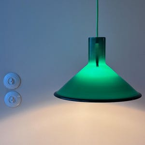 May include: A green glass pendant light fixture hangs from the ceiling. The light is on and casts a warm glow on the wall.