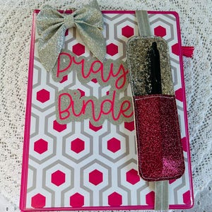May include: A pink and gray planner with a silver glitter bow, a pink glitter pen holder, and the words "Pray Bundle" in silver glitter letters.