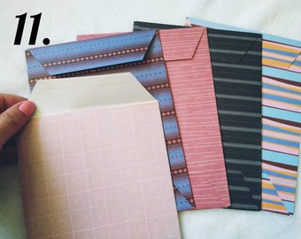 May include: A set of five decorative envelopes with different patterned designs. The envelopes are in shades of blue, pink, black, and brown. The envelopes are all closed and ready to be used.