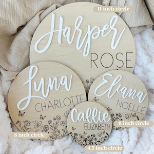 May include: A collection of personalized wooden name signs in various sizes: 11-inch, 8-inch, 6-inch, and 4.5-inch circles. Each sign features a name in white script, with additional names in a smaller font. Floral and butterfly designs are etched around the edges.
