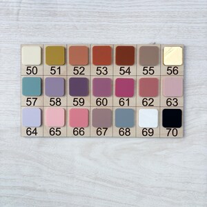 Puede incluir: Una tabla de muestras de color de madera con 20 muestras de pintura cuadradas. Los colores van del crema al negro, incluyendo tonos de amarillo, naranja, rojo, marr&oacute;n, morado, rosa, azul y dorado. Cada color est&aacute; numerado del 50 al 70.