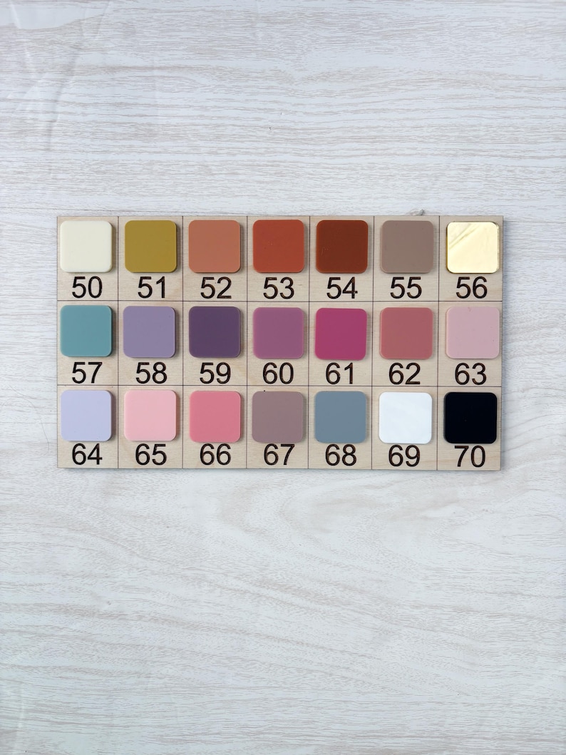 Puede incluir: Una tabla de muestras de color de madera con 20 muestras de pintura cuadradas. Los colores van del crema al negro, incluyendo tonos de amarillo, naranja, rojo, marr&oacute;n, morado, rosa, azul y dorado. Cada color est&aacute; numerado del 50 al 70.