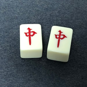 Puede incluir: Dos fichas de mahjong blancas con caracteres chinos rojos. Los caracteres son los mismos en ambas fichas.