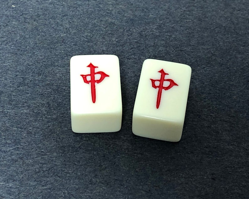 Puede incluir: Dos fichas de mahjong blancas con caracteres chinos rojos. Los caracteres son los mismos en ambas fichas.
