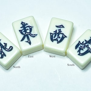 Puede incluir: Cuatro fichas de mahjong blancas con caracteres chinos negros. Las fichas representan las cuatro direcciones: Norte, Este, Sur y Oeste.