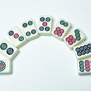 Puede incluir: Un juego de diez fichas de domin&oacute; blancas con puntos negros y rojos dispuestos en semic&iacute;rculo sobre una superficie blanca.