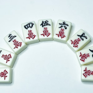 Puede incluir: Un conjunto de diez fichas de mahjong blancas con caracteres chinos negros y rojos. Las fichas est&aacute;n dispuestas en forma de semic&iacute;rculo.