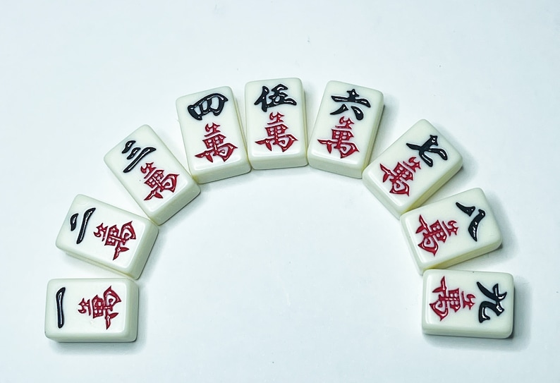 Puede incluir: Un conjunto de diez fichas de mahjong blancas con caracteres chinos negros y rojos. Las fichas est&aacute;n dispuestas en forma de semic&iacute;rculo.