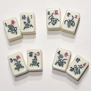 Puede incluir: Un juego de diez fichas de mahjong blancas con caracteres y s&iacute;mbolos chinos negros y rojos. Las fichas est&aacute;n numeradas del 1 al 4 y presentan diferentes dise&ntilde;os florales.