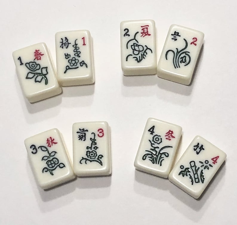 Puede incluir: Un juego de diez fichas de mahjong blancas con caracteres y s&iacute;mbolos chinos negros y rojos. Las fichas est&aacute;n numeradas del 1 al 4 y presentan diferentes dise&ntilde;os florales.