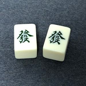 Puede incluir: Dos fichas blancas de mahjong con caracteres chinos negros en ellas. Los caracteres son "發", que significa "prosperidad" en ingl&eacute;s.
