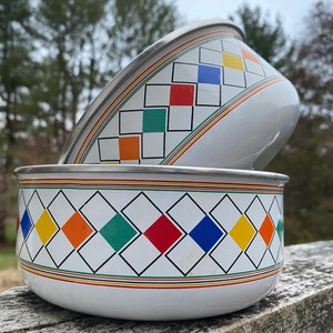 May include: Two white bowls with a geometric design. The bowls have a silver rim and are decorated with colorful diamonds in red, yellow, green, and blue. The bowls are stacked on top of each other.