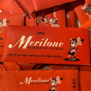 May include: A collection of vintage red Meritone phonograph needle boxes. The boxes feature the brand name in white script, a cartoon character, and text that reads "Play 12 or more records with High Fidelity."