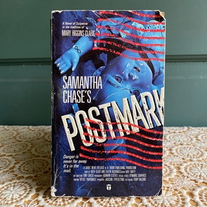 May include: A paperback book cover with a blue and red striped background. The title is "Samantha Chase's Postmark" and the author is Mary Higgins Clark. The cover features a doll with an infinity symbol on its arm.