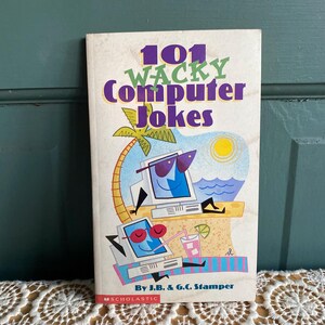 May include: A book titled "101 Wacky Computer Jokes" by J.B. & G.C. Stamper. The cover features a cartoon illustration of two computers on a beach, one wearing sunglasses and the other with pink sunglasses. The book is published by Scholastic.