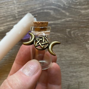 May include: A small glass bottle with a cork stopper and a charm attached. The charm is a gold-colored pentacle with three crescent moons on either side.