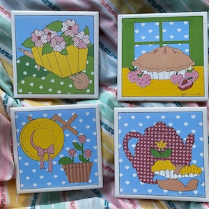 May include: Set of four colorful ceramic tiles featuring a variety of designs. The tiles feature a wheelbarrow with flowers, a pie in a window, a straw hat with a bow, and a teapot with a flower.