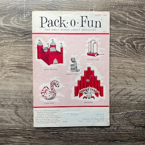 May include: A vintage magazine cover for Pack-o-Fun, a scrap-craft magazine from March 1966. The cover features illustrations of various crafts, including a castle, a dragon, a shoelace craft, a macaroni craft, and a centerpiece.