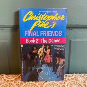 May include: A paperback book titled "Christopher Pike's Final Friends Book 2: The Dance." The cover is blue with yellow text and features a group of people in formal attire. The book's title is in pink.