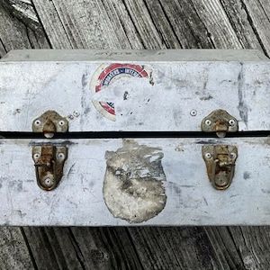 May include: A silver metal box with two latches and a sticker that says "Workers International" on the top. The box is slightly weathered and has a few scratches.