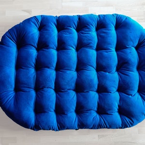 May include: A large, round, blue velvet cushion with a tufted design. The cushion is perfect for adding a touch of comfort and style to any room.