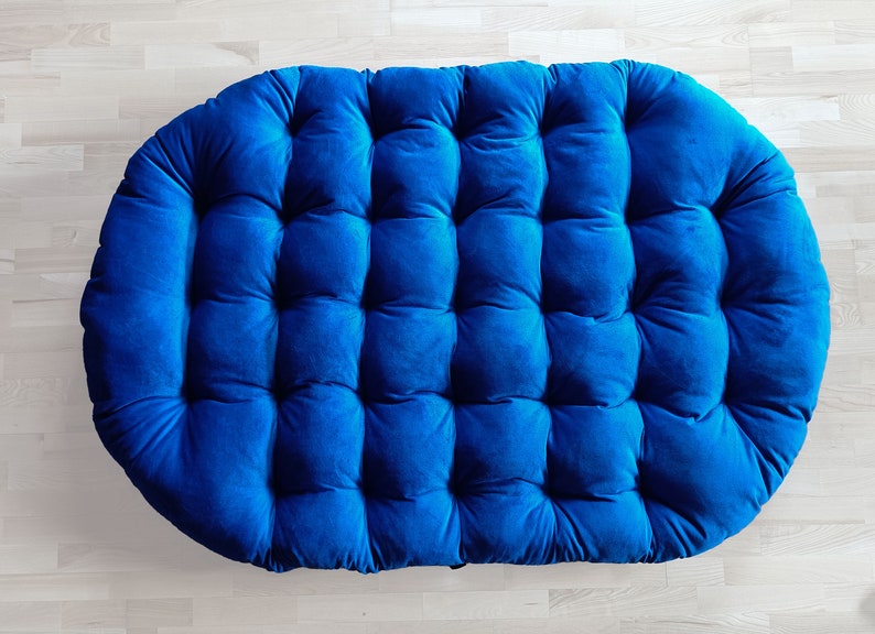 May include: A large, round, blue velvet cushion with a tufted design. The cushion is perfect for adding a touch of comfort and style to any room.