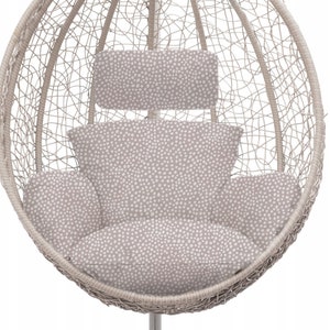 May include: A white wicker egg-shaped hanging chair with a beige cushion and a matching headrest. The cushion and headrest have a white polka dot pattern.
