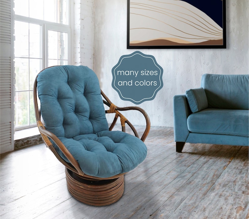 May include: A blue swivel chair with a padded cushion. The chair is made of woven rattan and has a wooden base. The chair is in a room with a white wall and a window in the background. The text "many sizes and colours" is visible in the image.