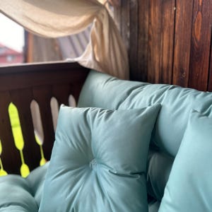 May include: A light blue cushion with a button detail and a white sheer curtain in the background.